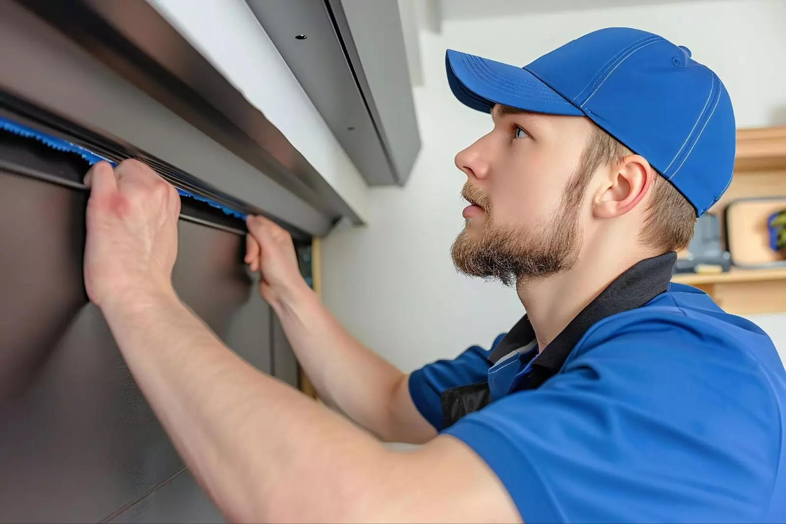 A man in a blue shirt and hat repairs a garage door, focusing on weather stripping and insulation improvements.