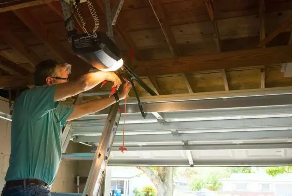 A man is repairing a garage door opener focused on the mechanism with tools in hand